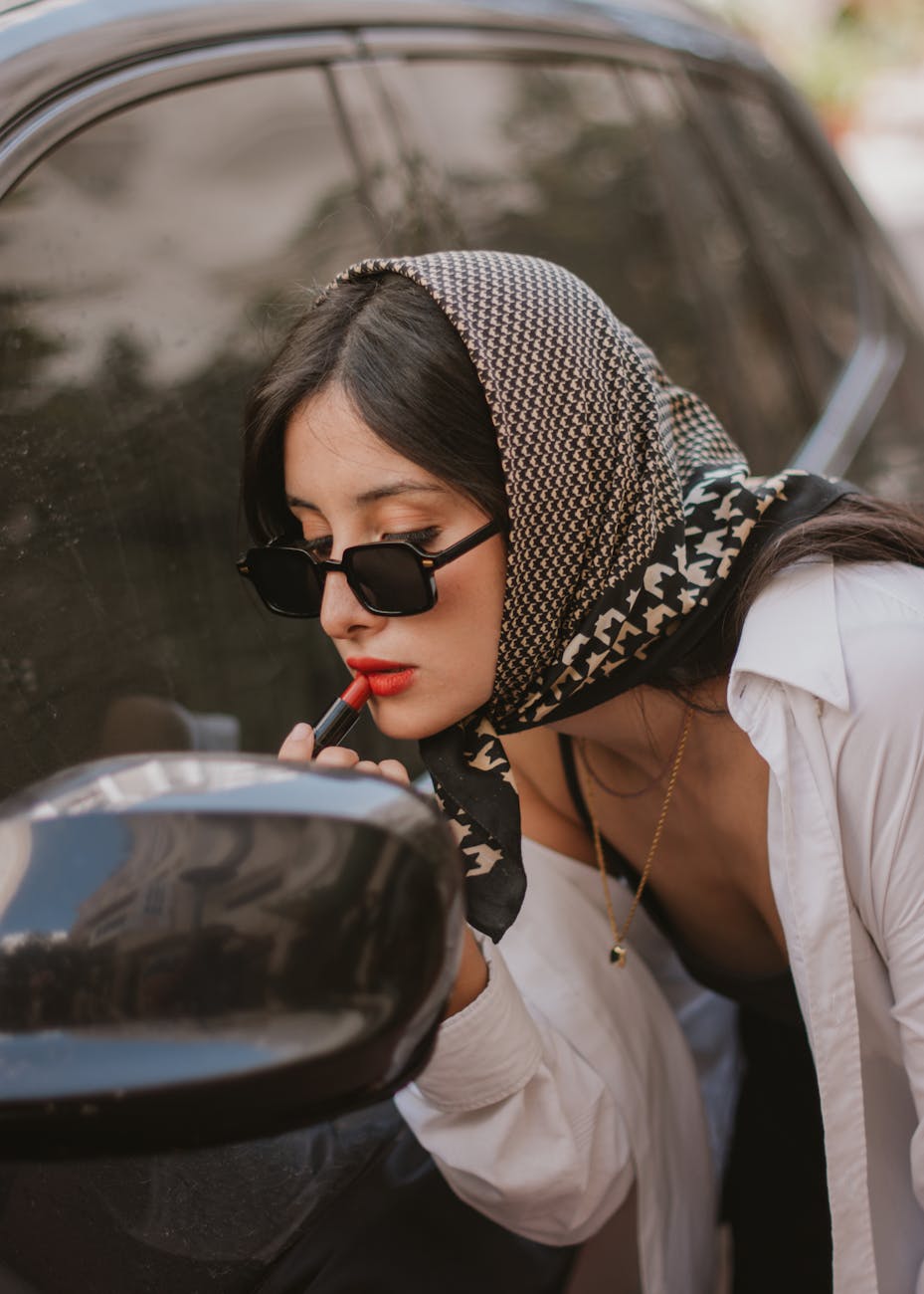 elegant woman doing makeup by the car mirror