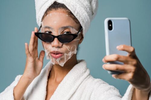 confident black female with sheet mask taking selfie on smartphone